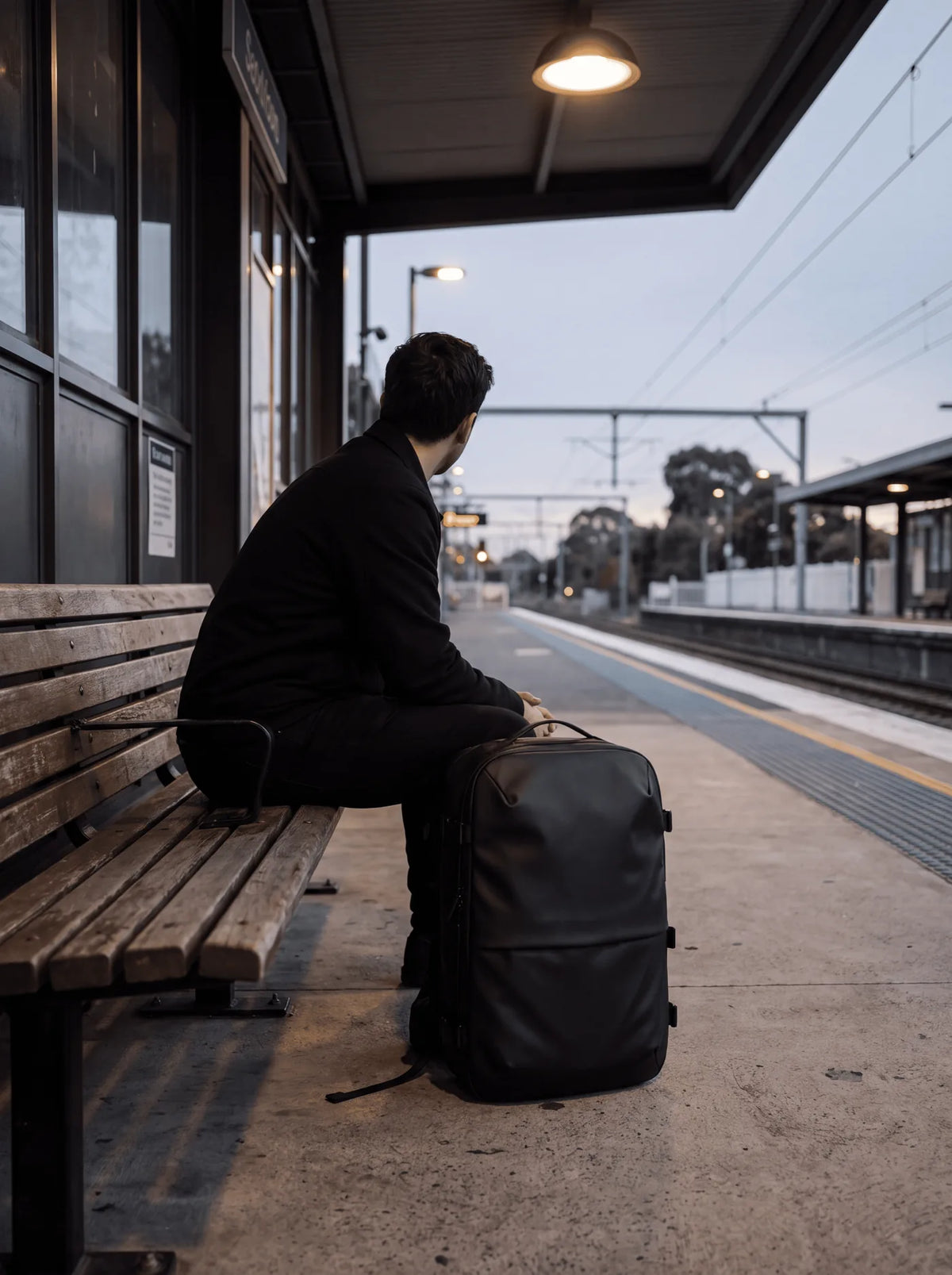 A traveller waits on an empty railway platform at dusk, ProPack beside them
